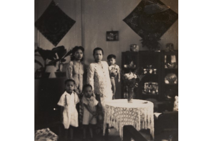 <a href="/assets/3024b79a-f2b0-4336-b0d1-45682856b8da/Abdul Latiff and Hajjah Fatimah.jpg">Abdul Latiff bin Omar (seated in the middle) with his mother Hajjah Fatimah (seated to his left) and his father Haji Omar (standing on the left) in their home, which has been furnished with objects from South Kalimantan</a>